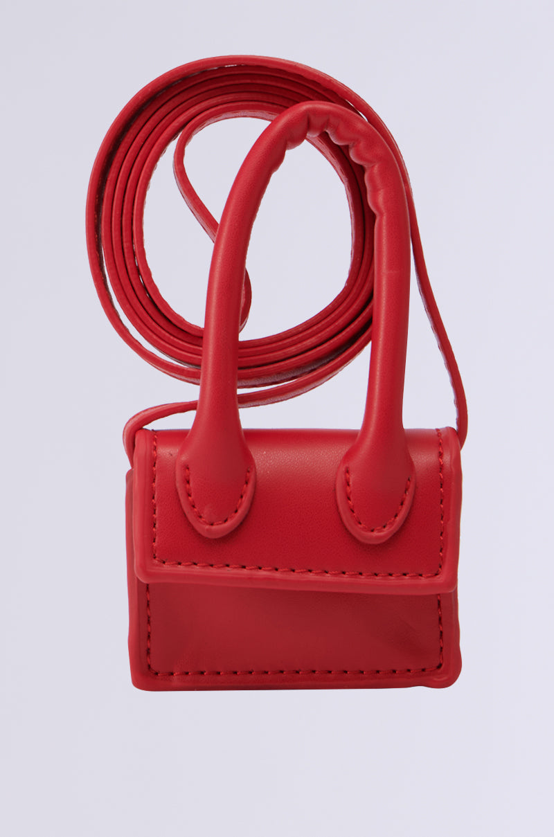 A small red RUNWAY CHIC BAG BRACELET made of faux leather, featuring detailed stitching, two handles, and a long, thin strap is displayed against a plain white background.