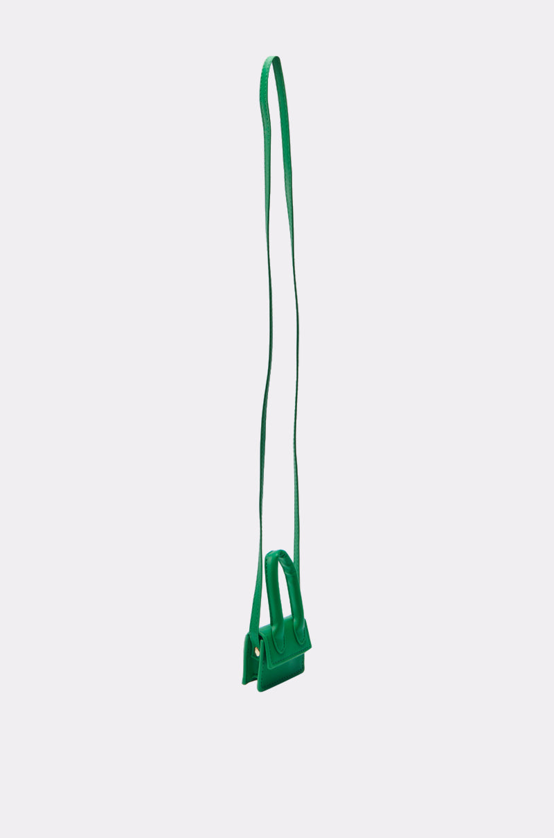 The IN MY BAG BRACELET, a small green faux leather handbag with a long shoulder strap, is shown against a light gray background—a stylish multifunctional accessory for any occasion.
