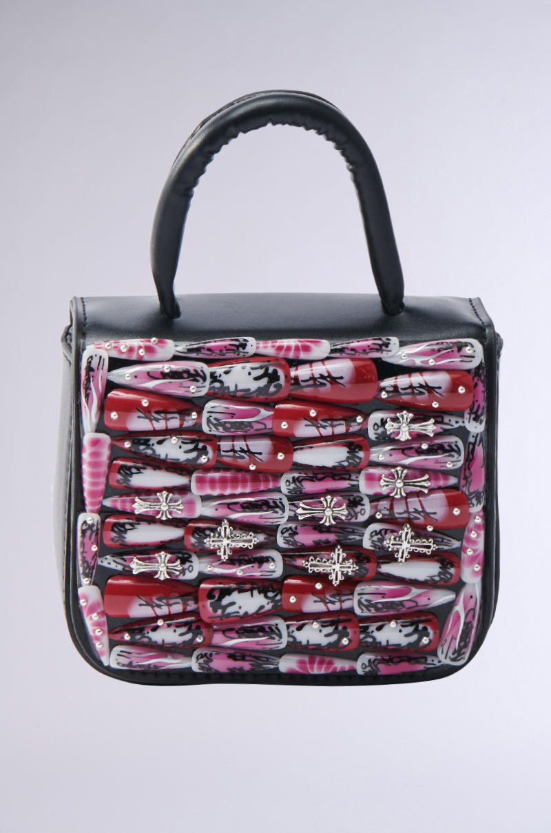 The NAILED IT PURSE is a mini square bag in black faux leather, detailed with glossy red, pink, and white nail art accents plus metallic insect and cross charms for a bold, edgy style.