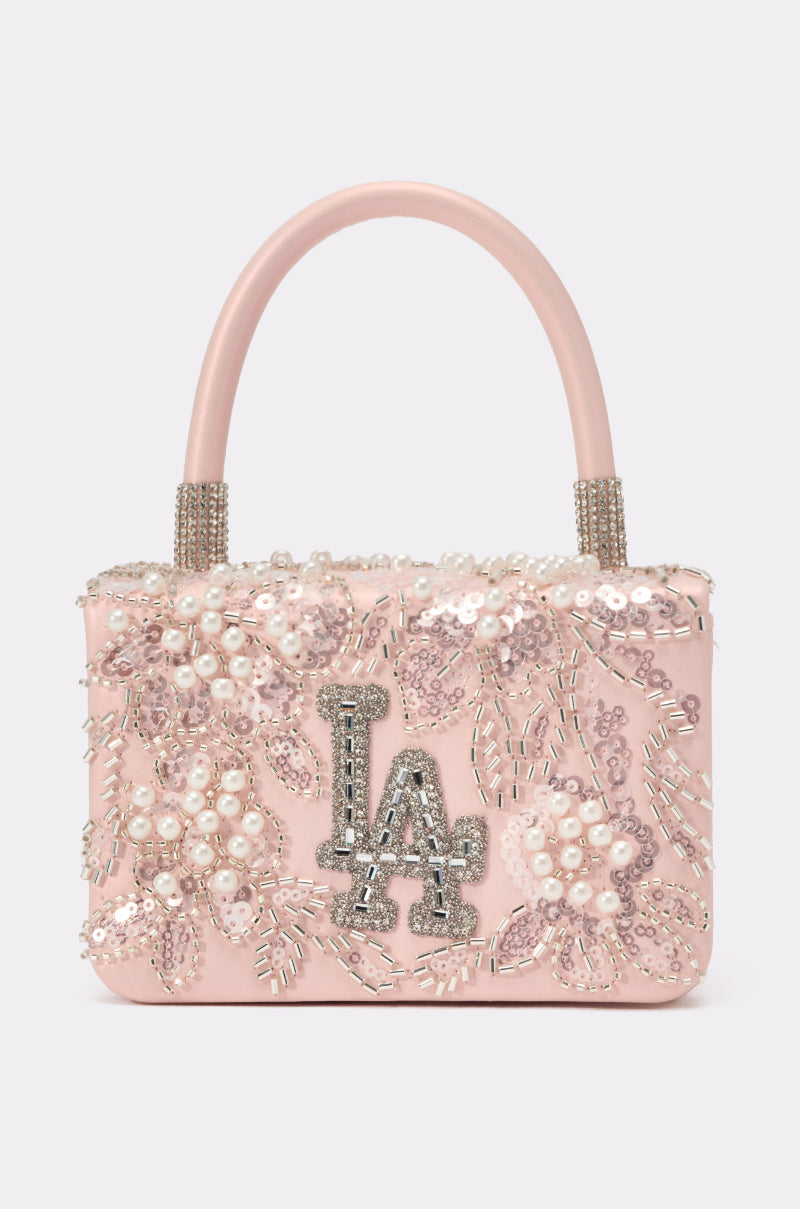 The HEARD U PURSE is a small pale pink faux leather mini handbag with beaded floral embroidery, pearl accents, silver "LA" logo on the front, two short handles, and detailed decorative elements. 0