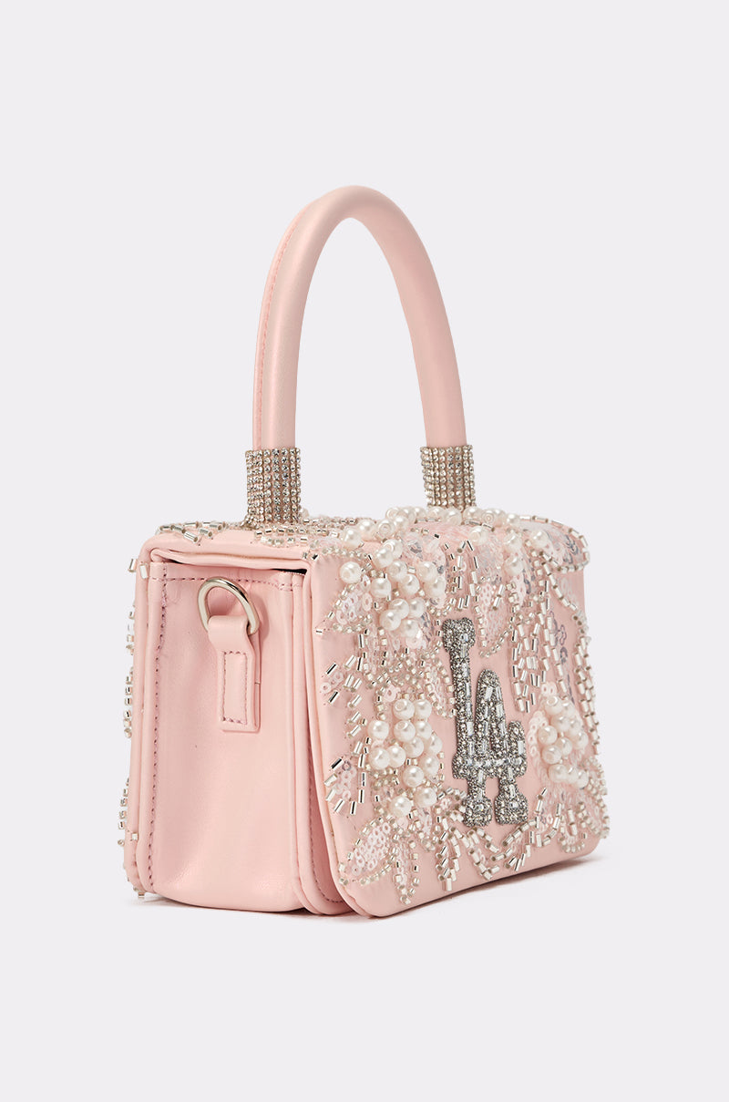 The HEARD U PURSE is a pink faux leather mini handbag with dual handles, decorated with pearl and crystal bead floral embellishments and a sparkling silver rhinestone “LA” logo—perfect as a chic courtside accessory. 3