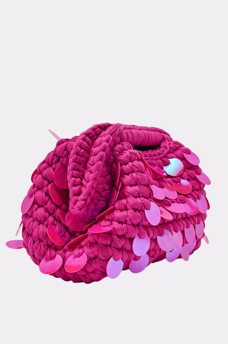 The ITS MY WORLD CROCHET SEQUIN CLUTCH is a bright pink, chunky knit Y2K-inspired bag featuring large shiny sequins and a braided handle, shown against a plain white background. 3