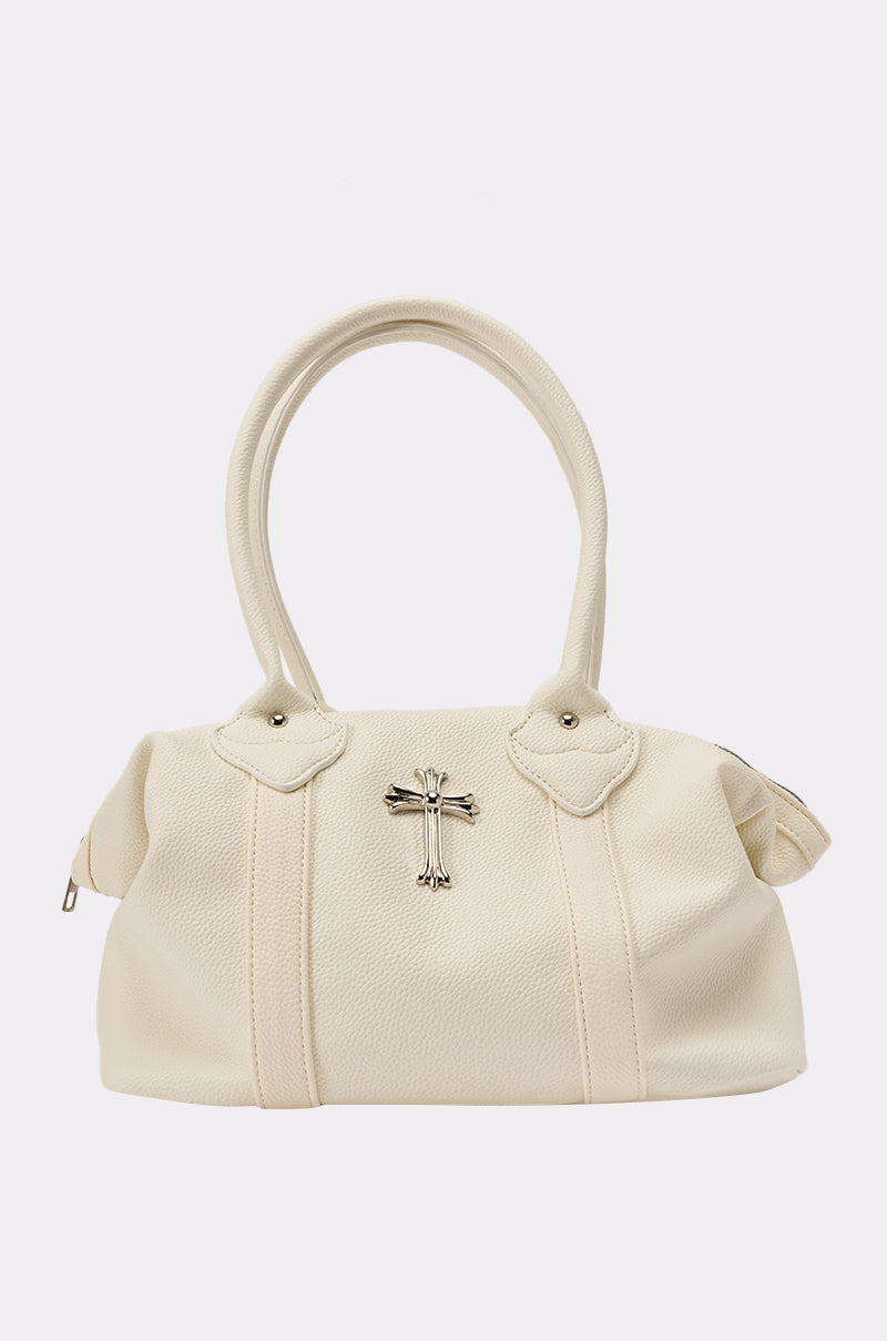 The WITH IT SNAP BAG is a cream oversized faux leather shoulder bag with two rounded handles, subtle texture, silver-tone hardware, and a silver cross emblem on the front, shown against a plain white background. 2