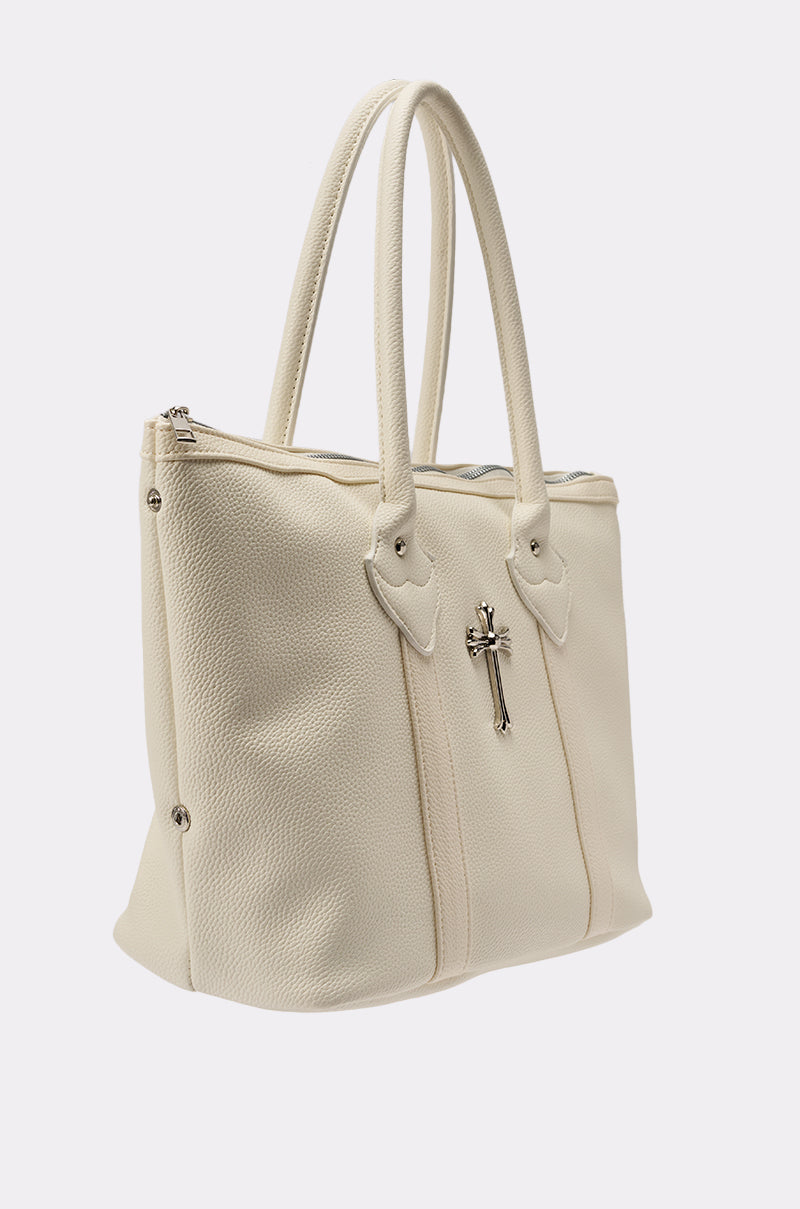 The WITH IT SNAP BAG is a cream-colored, oversized faux leather shoulder bag with double handles, silver-tone hardware, and a decorative cross charm on the front. 3