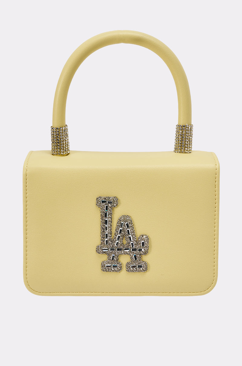 The IN THE SUN BLING PURSE is a small, rectangular pale yellow handbag featuring a rounded handle and sparkling silver rhinestone "LA" lettering on the front. 1