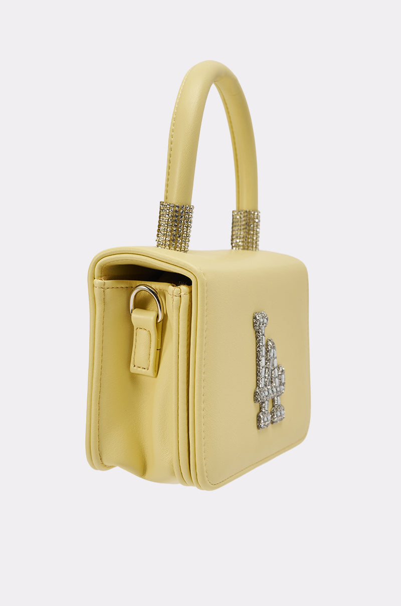 The IN THE SUN BLING PURSE is a small, structured yellow handbag with a top handle adorned with rhinestones, a sparkling "L" emblem on the front, smooth sides, and metallic hardware. 3