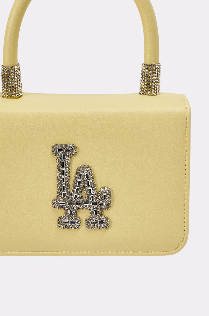 A close-up of the IN THE SUN BLING PURSE, a pastel yellow handbag featuring beaded handles and a sparkling, rhinestone-encrusted "LA" logo on the front. 4