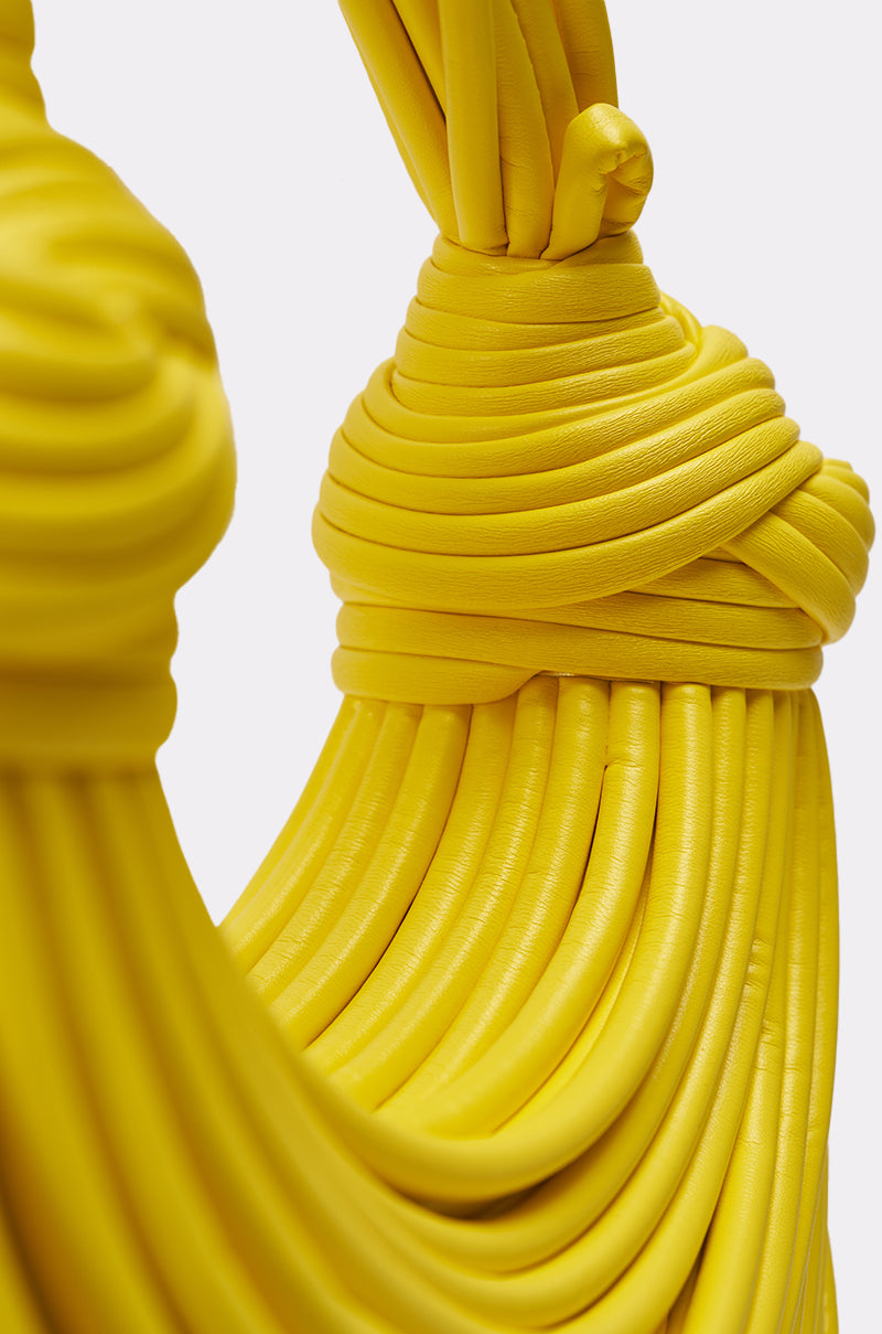 Close-up of the BANANA SPLIT WHO PURSE, a bold yellow fringe handbag with a coiled, textured design in smooth tubular faux leather, featuring intricate wrapped and layered details against a plain white background. 3