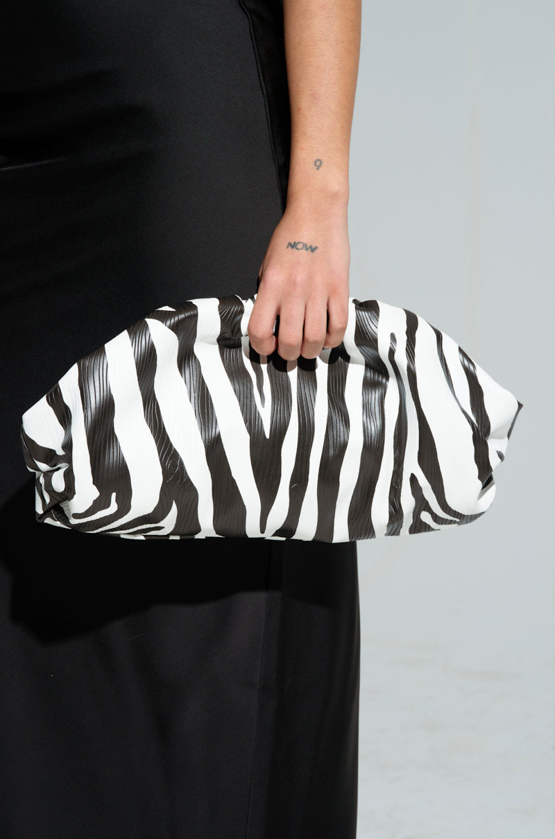 A person in a black dress holds the striking "Into the Wild Zebra Clutch" made from faux leather, their wrist adorned with a small tattoo.