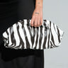 A person in a black dress holds the striking "Into the Wild Zebra Clutch" made from faux leather, their wrist adorned with a small tattoo.