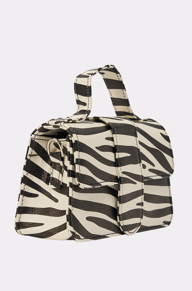 The LETS GET WILD ZEBRA BAG is a structured mini bag with a bold zebra print, featuring a top handle and front flap closure that stands out against any plain light background. 2