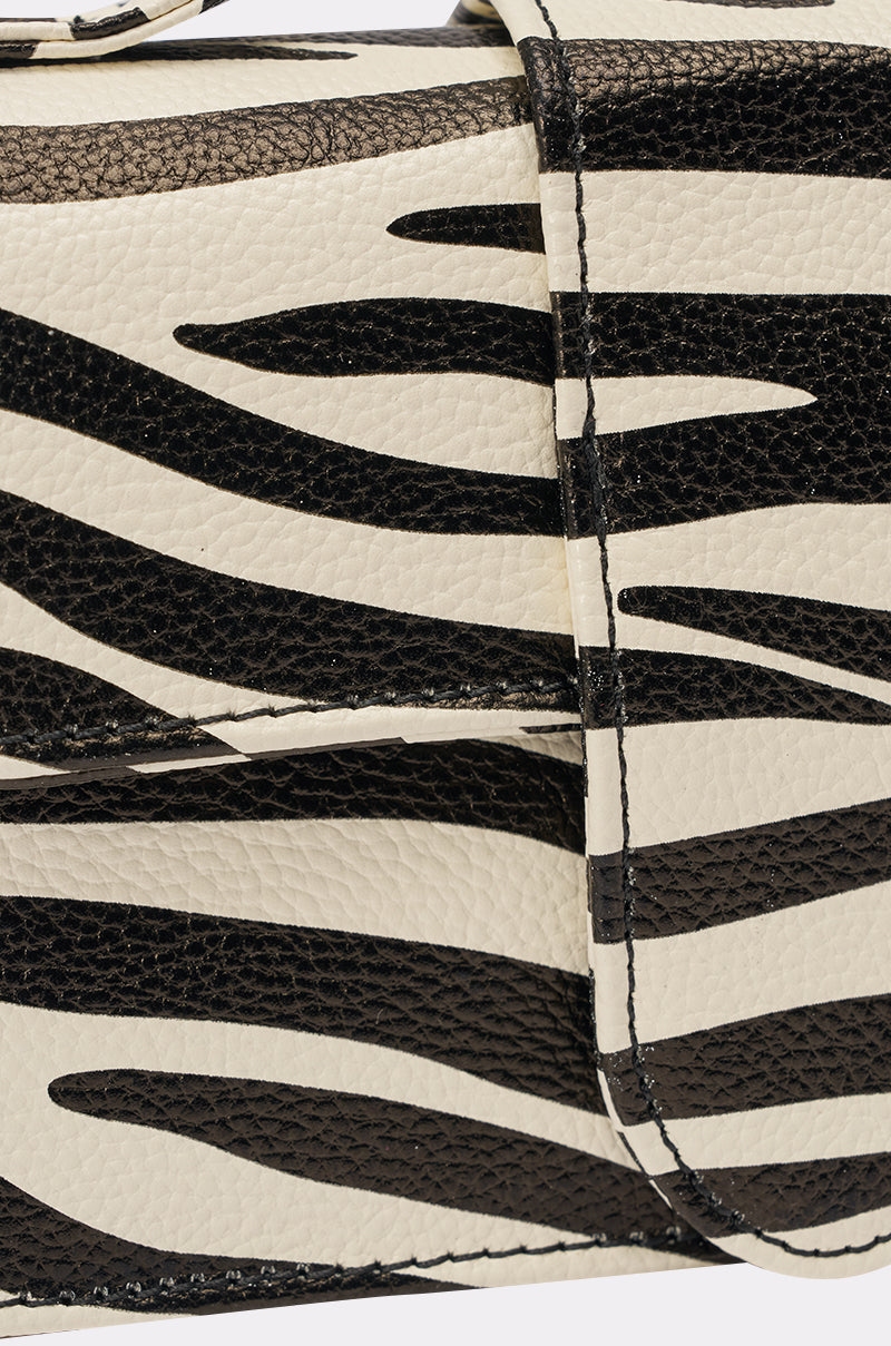 Close-up of the LETS GET WILD ZEBRA BAG, a structured mini bag featuring textured leather with a zebra print and visible stitching on the strap and flap. 3
