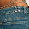 Close-up of a person wearing jeans enhanced by the BLING LIFE PANT ADJUSTER, featuring intricate button details and sparkling rhinestone embellishments. A tattoo and a chain with circular ornaments are visible above the waistband. The focus is on the texture, design elements, and the perfect fit provided by both the clothing and accessories.