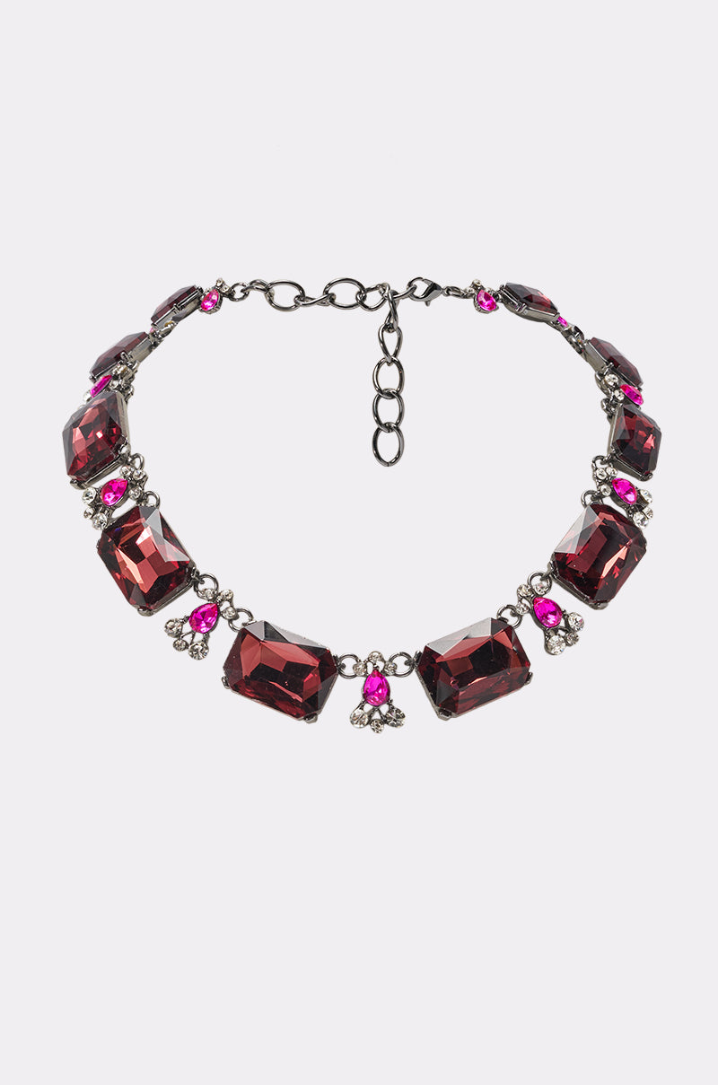 The KEKE NECKLACE showcases large rectangular deep red stones, round pink gems, and small clear crystals on a dark metal chain with adjustable clasp—an elegant accessory to elevate any evening look.