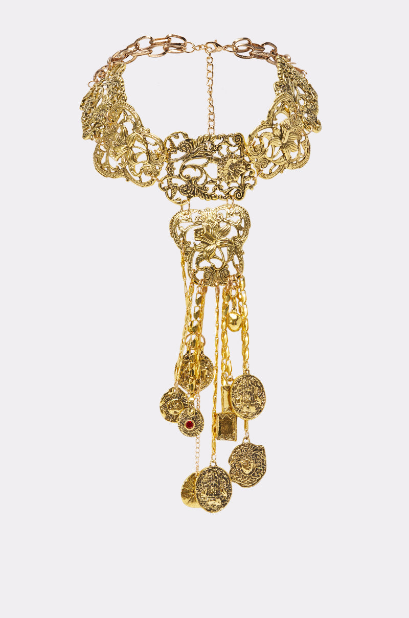 The ARTSY NECKLACE features a gold filigree design with dangling chains and red gemstone medallions, offering vintage charm that stands out beautifully against a plain white background.
