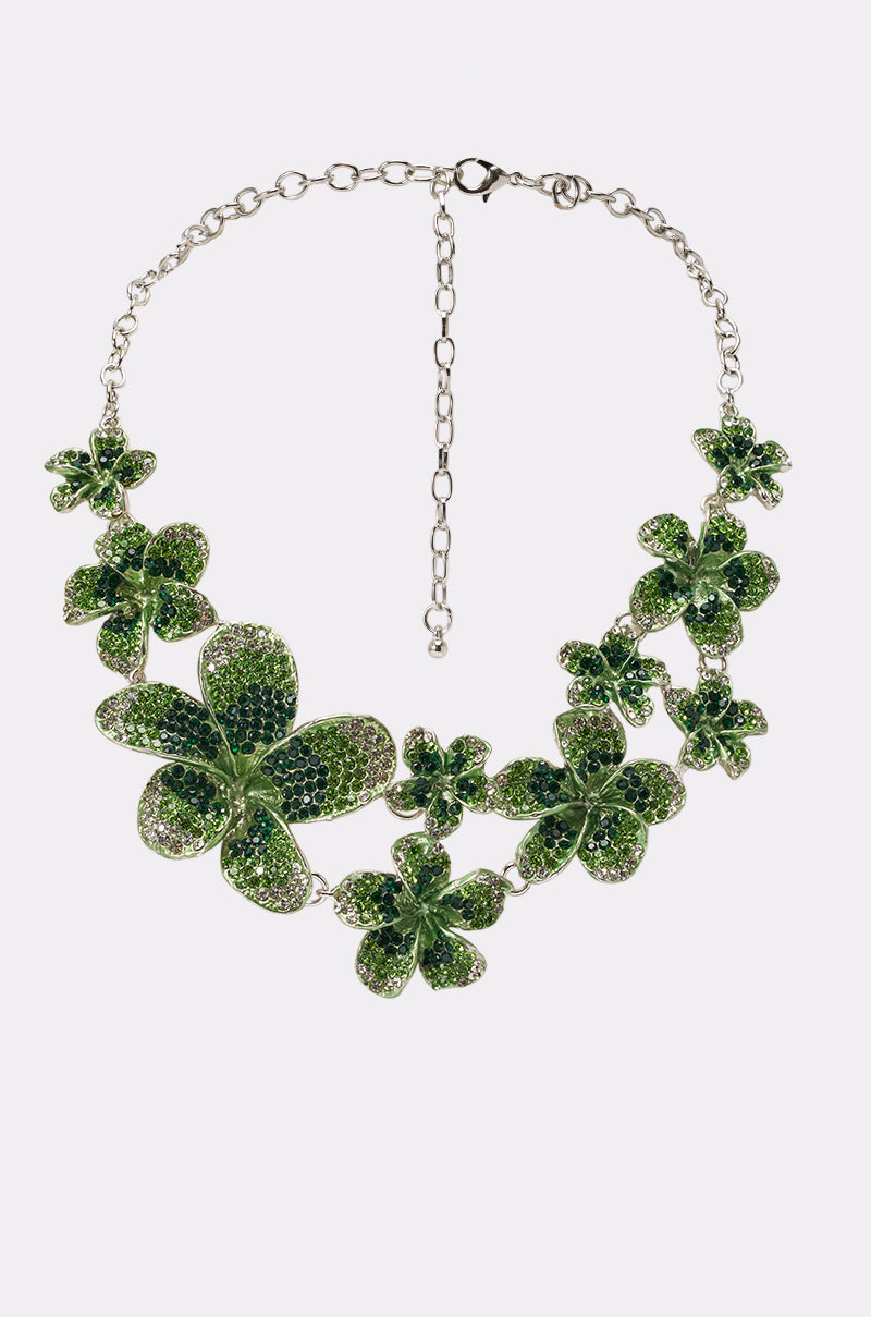 The TO THE GARDEN STATEMENT NECKLACE showcases silver chains with large and small green, crystal-encrusted blooms arranged asymmetrically, plus an adjustable clasp—ideal bold jewelry for any vacation.