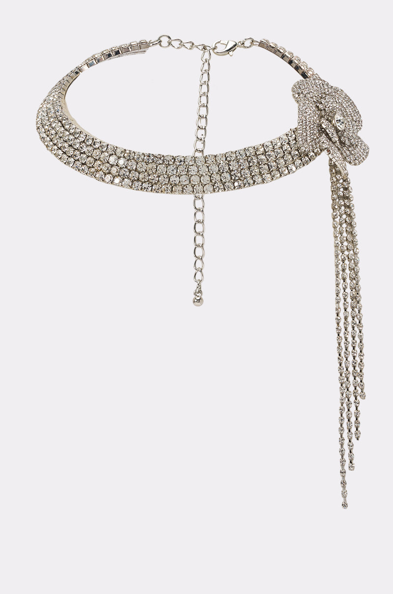 The ALEXA NECKLACE is a silver rhinestone collar necklace featuring a stunning floral accent on one side and cascading chain tassels, designed with an adjustable clasp closure for the perfect fit.