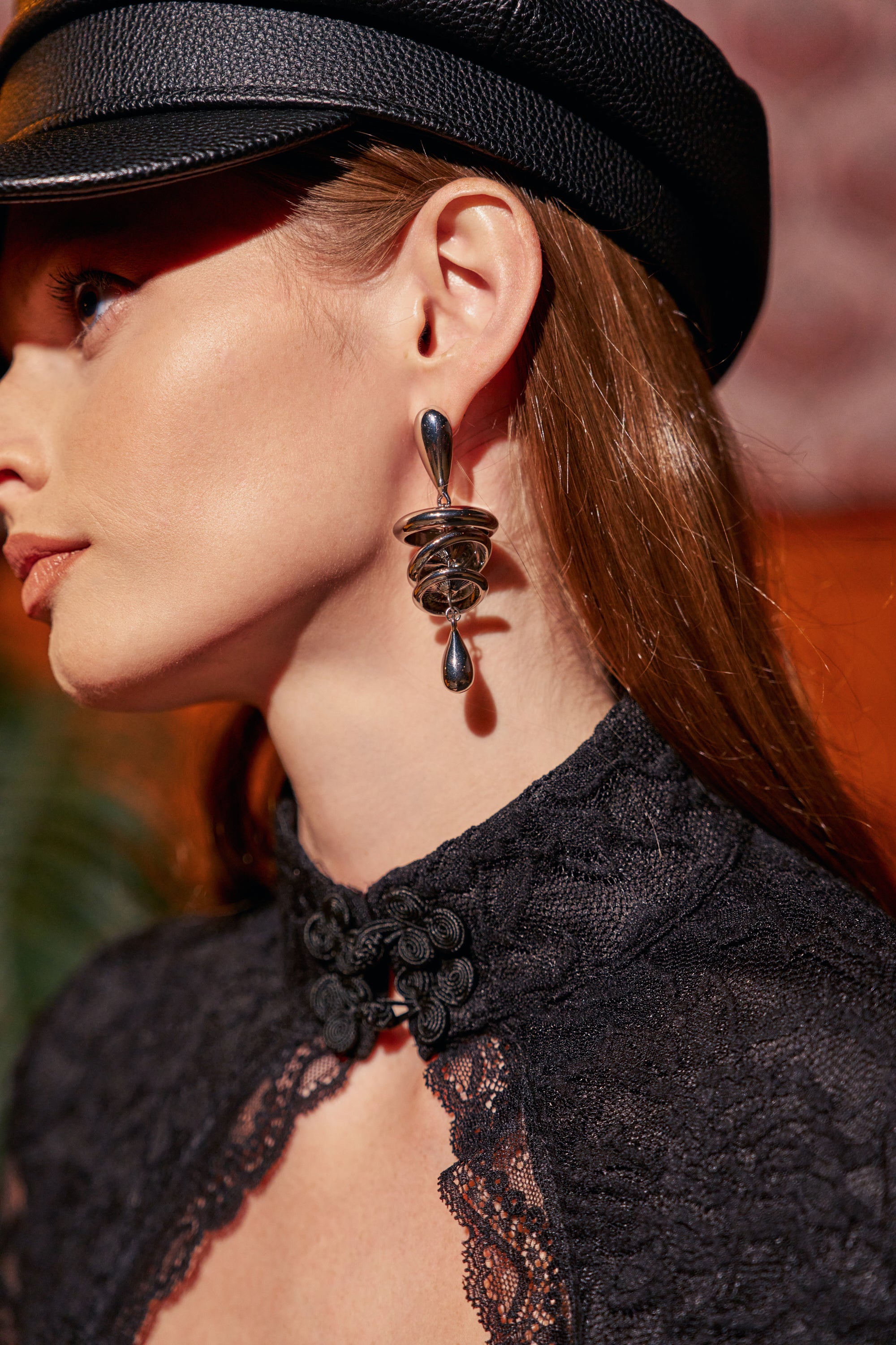 Profile view of a person wearing CHROME DROP EARRINGS, featuring a teardrop post and a swirling, coiled lower element.