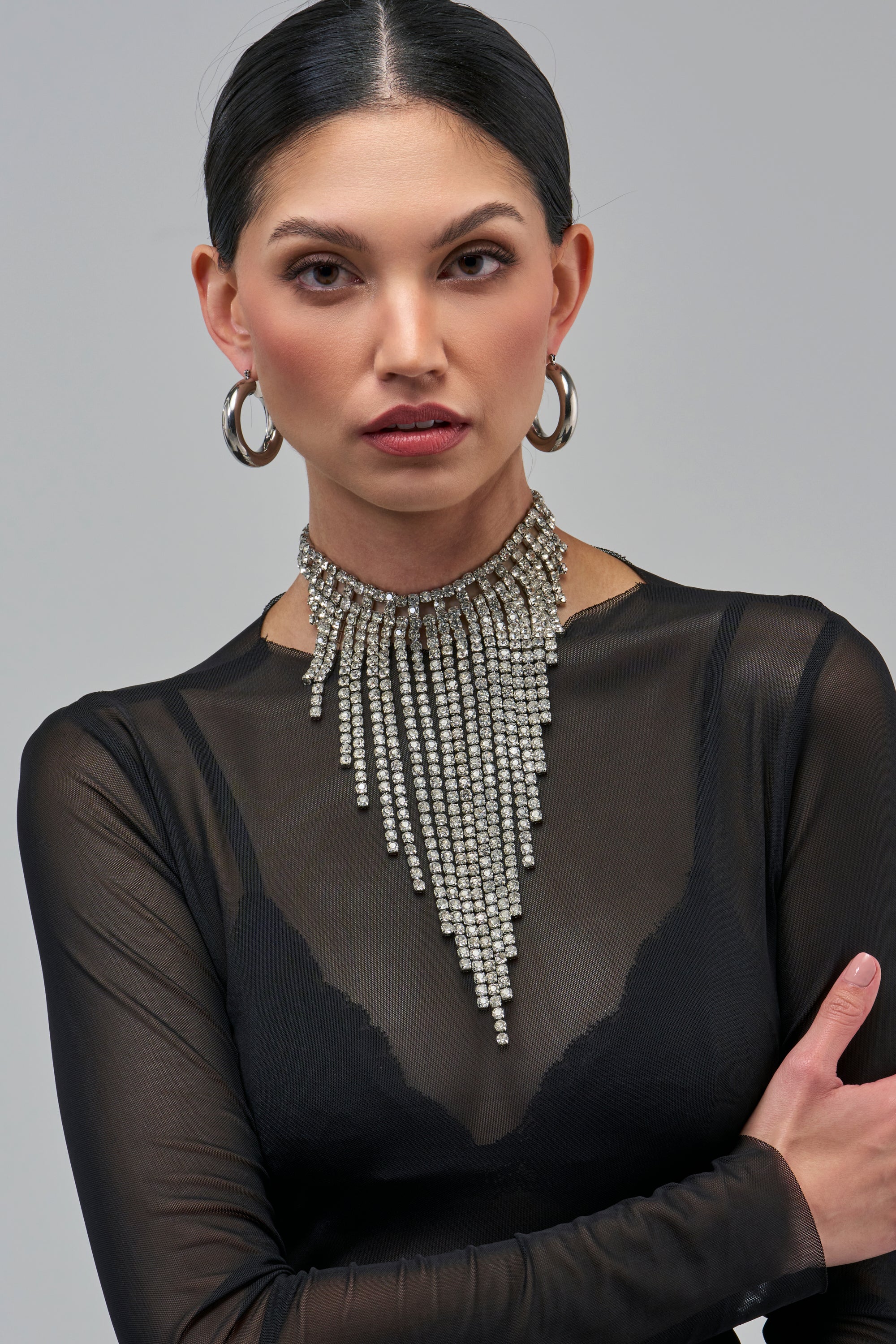 A model wearing a BLINGED OUT CRYSTAL NECKLACE, a silver statement piece with cascading rows of rhinestone fringe.