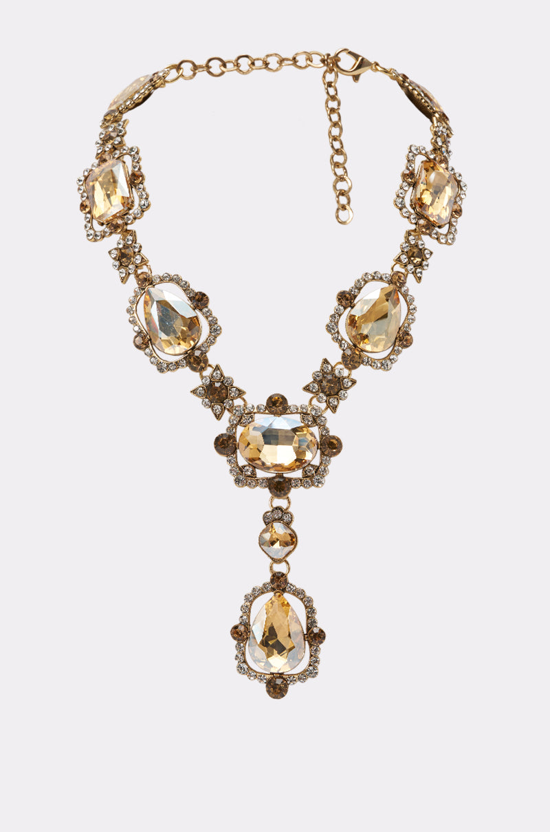 The ART DECO NECKLACE features large oval yellow gemstones, accented with clear and brown stones, ornate links, and an adjustable clasp—a striking piece that adds elegance to any outfit.