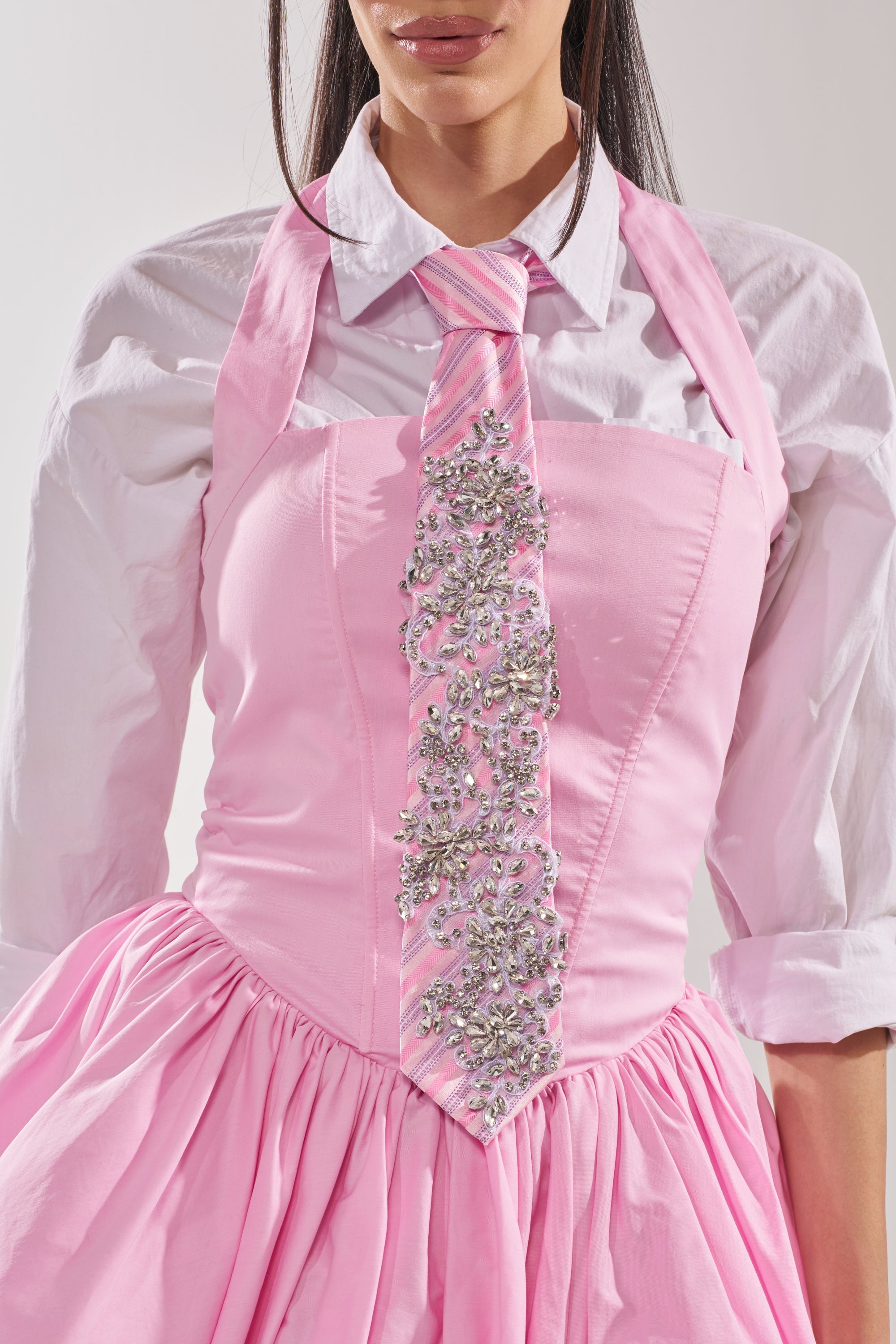 A woman wears a light pink corset dress over a white button-up shirt, paired with the pink crystal-embellished FEMME APPLIQUE TIE. Only her torso is visible. 0