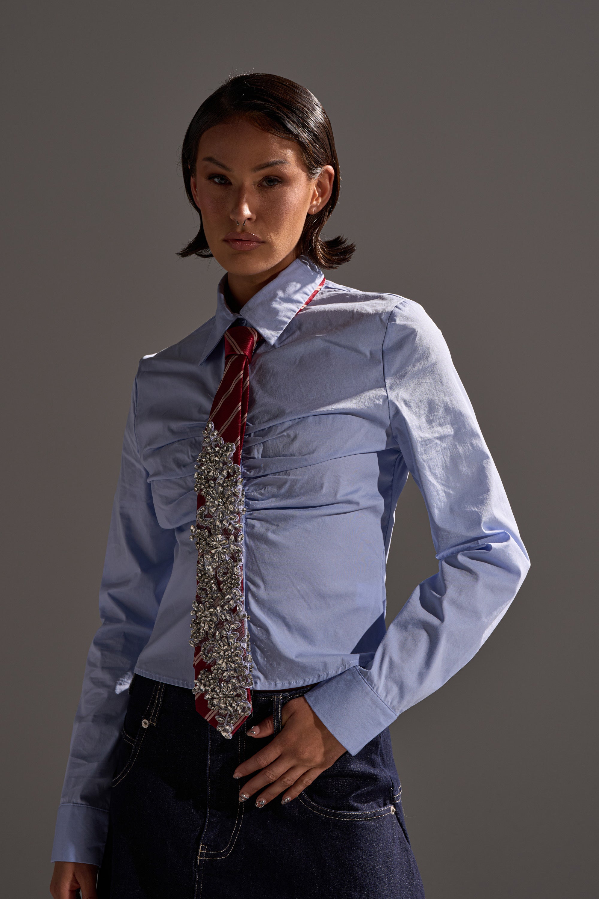 A person wearing a light blue button-up shirt, the NOT YOUR TYPICAL TIE IN RED, and a dark skirt stands confidently against a plain gray background. 1