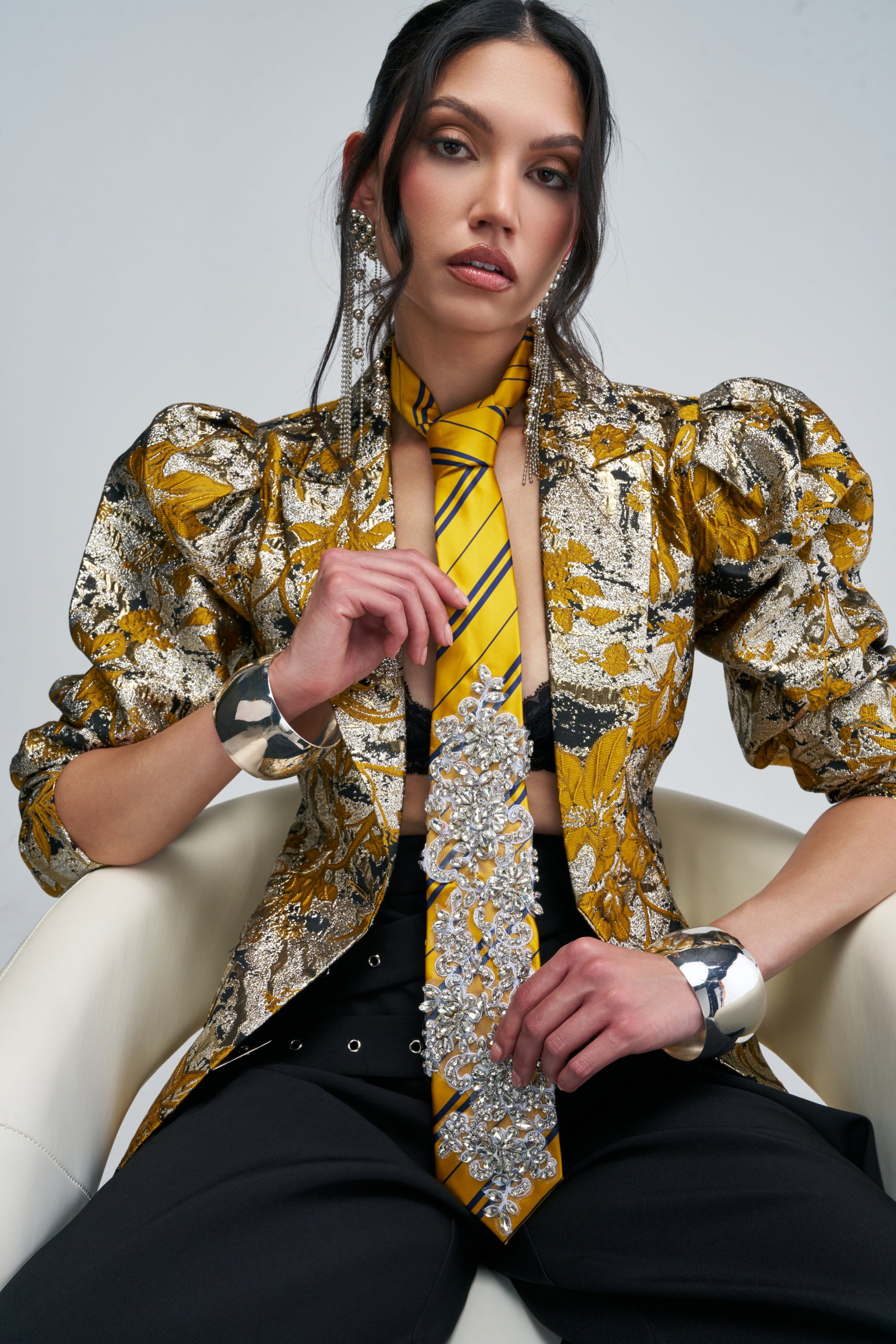 A person wearing a BUSINESS NOT CASUAL EMBELLISHED TIE in mustard, featuring blue stripes and intricate crystal accents down the center.