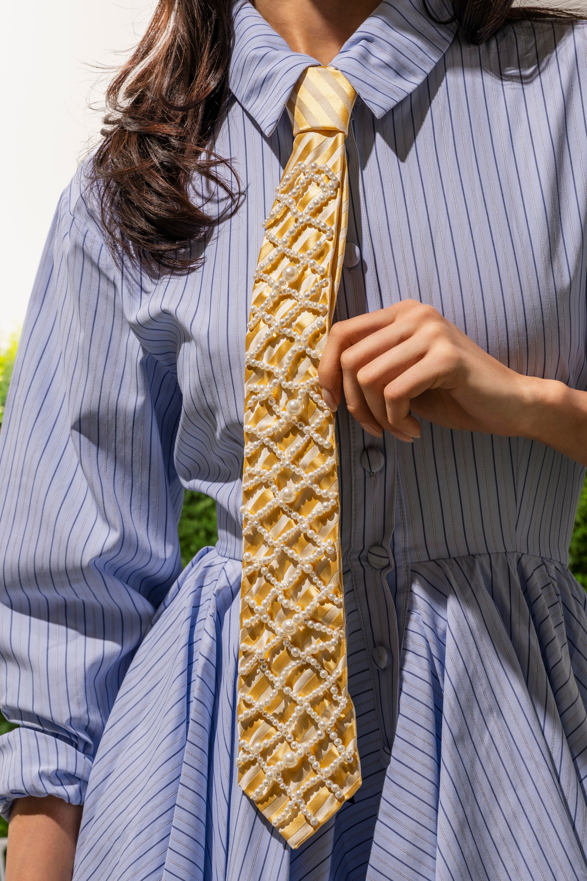 A person in a blue pinstripe dress with puffed sleeves holds the FEMME APPLIQUE TIE, a butter yellow necktie featuring intricate white beadwork. The person's face is not visible. 0
