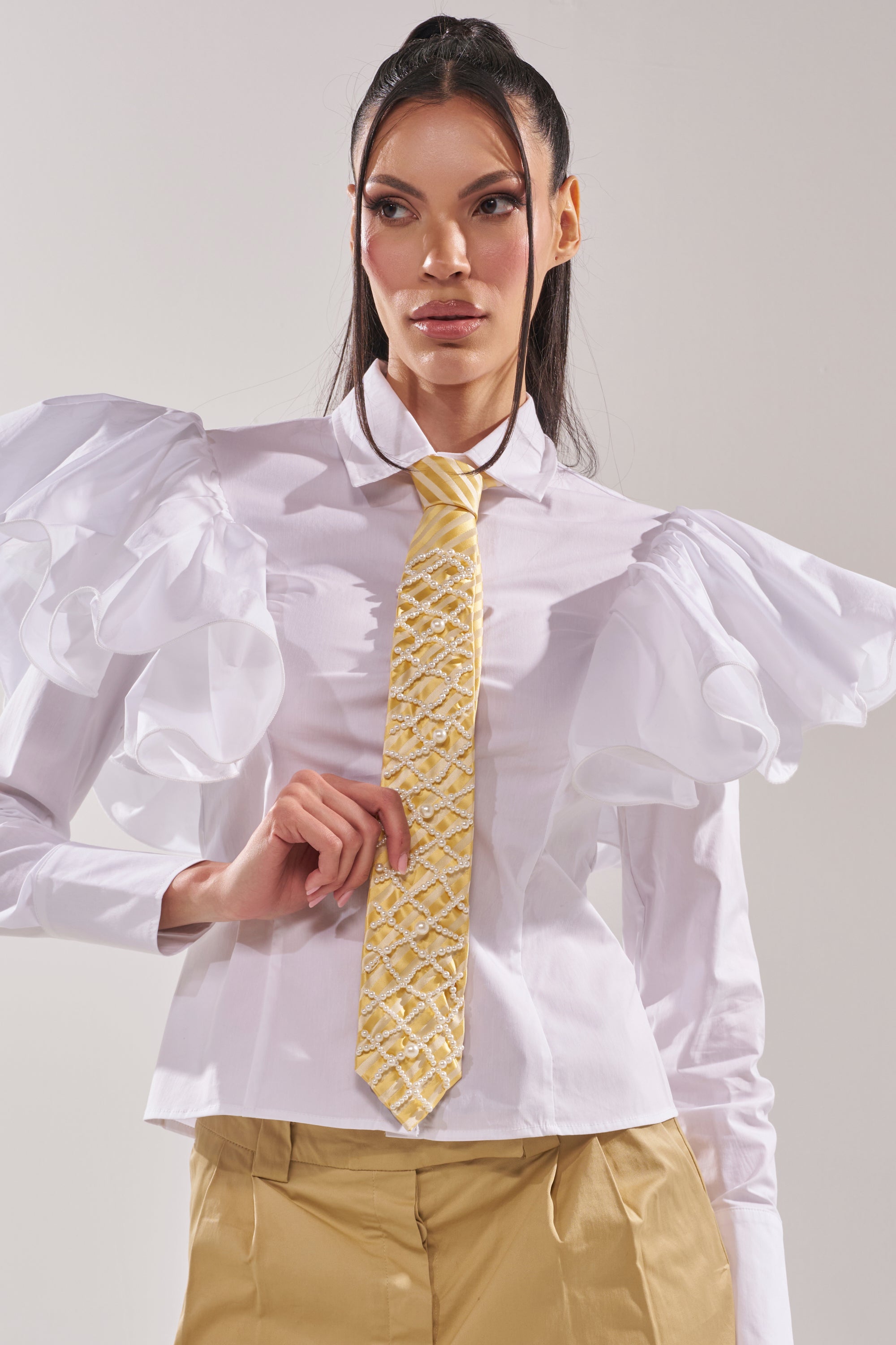 A woman wears a white shirt with large ruffled sleeves, tan pants, and the FEMME APPLIQUE TIE in butter yellow stripes. She poses confidently against a plain, light background. 1