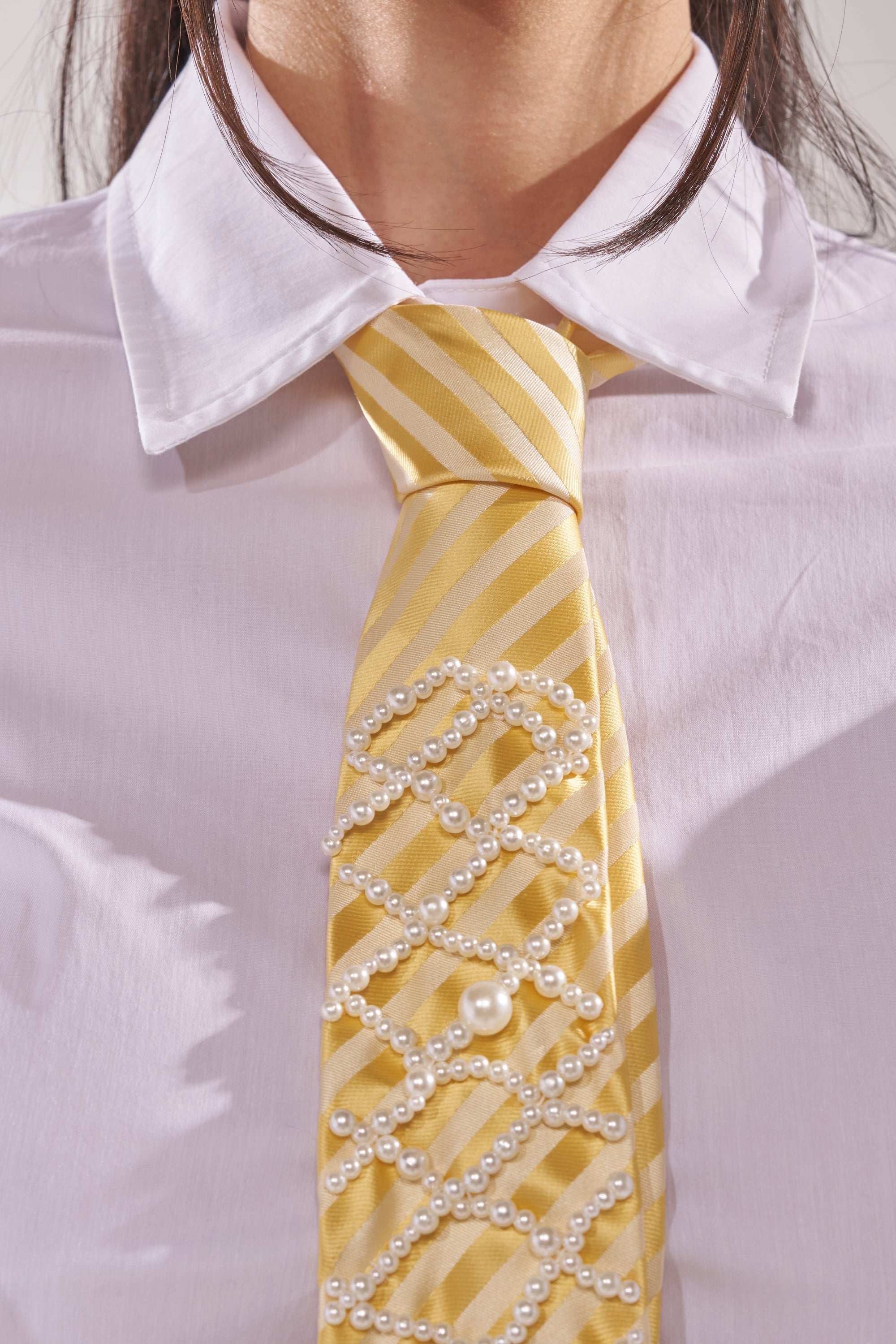 A person wears the FEMME APPLIQUE TIE, a yellow striped necktie with delicate pearl overlay, paired with a white collared shirt for an elegant and unique look. 8