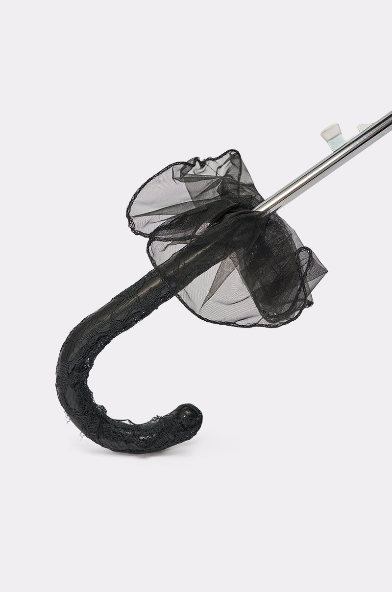 A close-up of the UNDER MY SPELL LACE UMBRELLA handle wrapped in black lace, featuring a sheer frilled fabric with a delicate scalloped edge near the base, set against a plain white background. 7