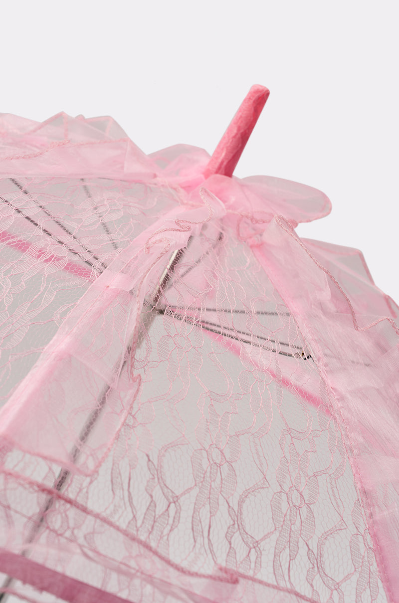 Close-up of the UNDER MY SPELL LACE UMBRELLA, featuring pink lace with scalloped edges, delicate floral patterns, and a fabric-covered handle, set against a plain light background. 2