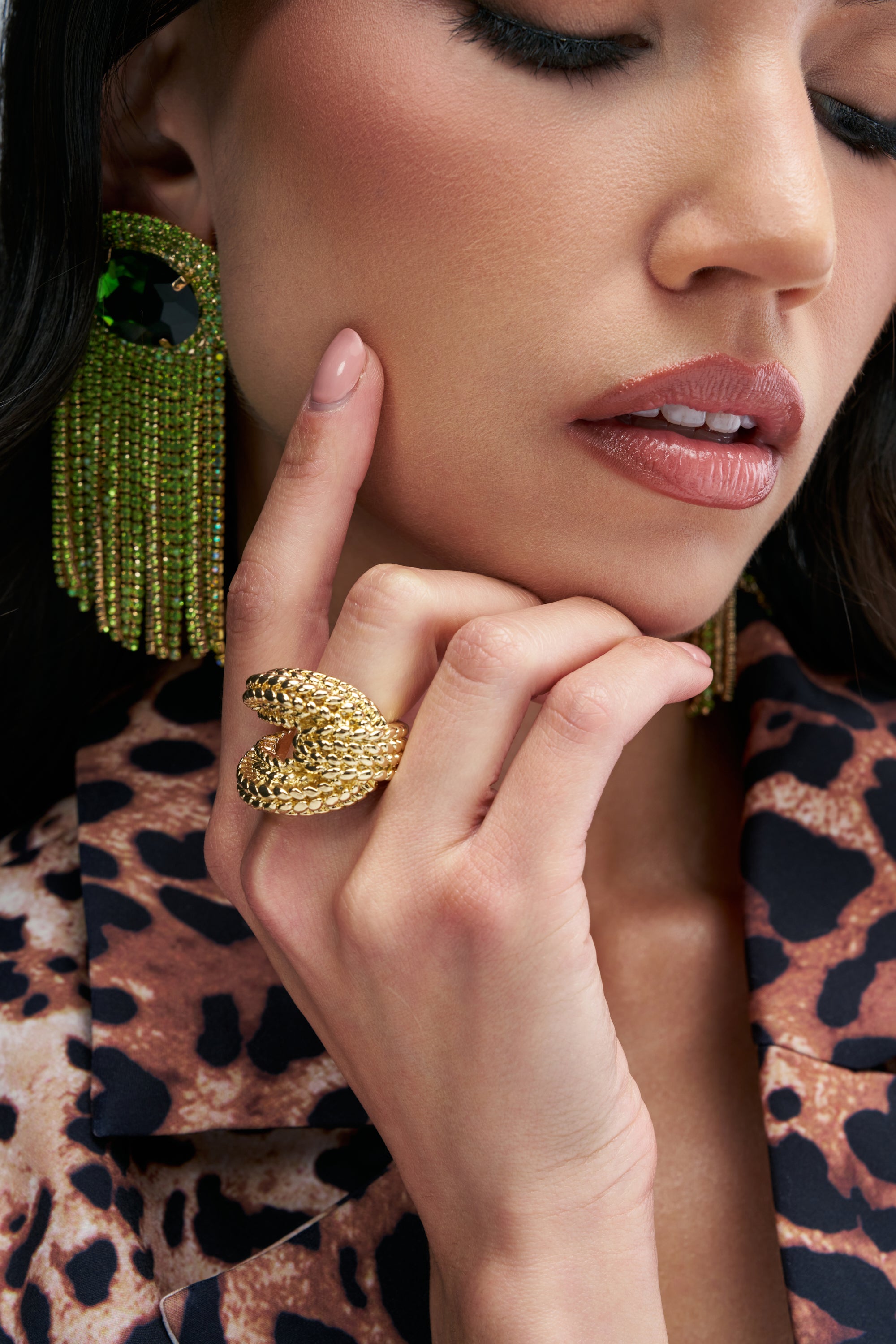 A person rests their chin against their hand, wearing a textured COBRA RING IN GOLD shaped like a coiled snake.