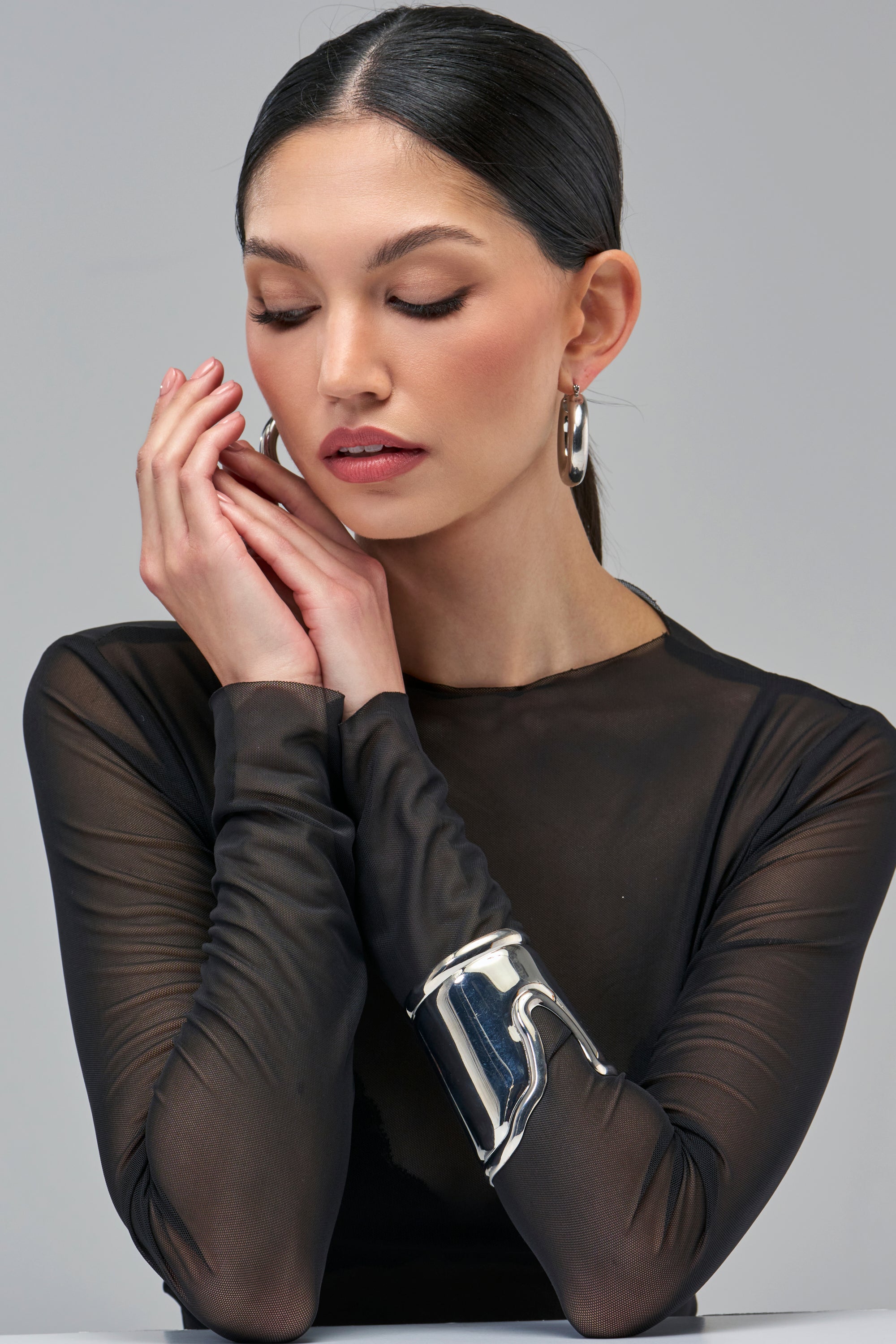 A person wears a wide, curved SILVER ARMOR CUFF BRACELET, a sculptural silver statement accessory on their forearm.