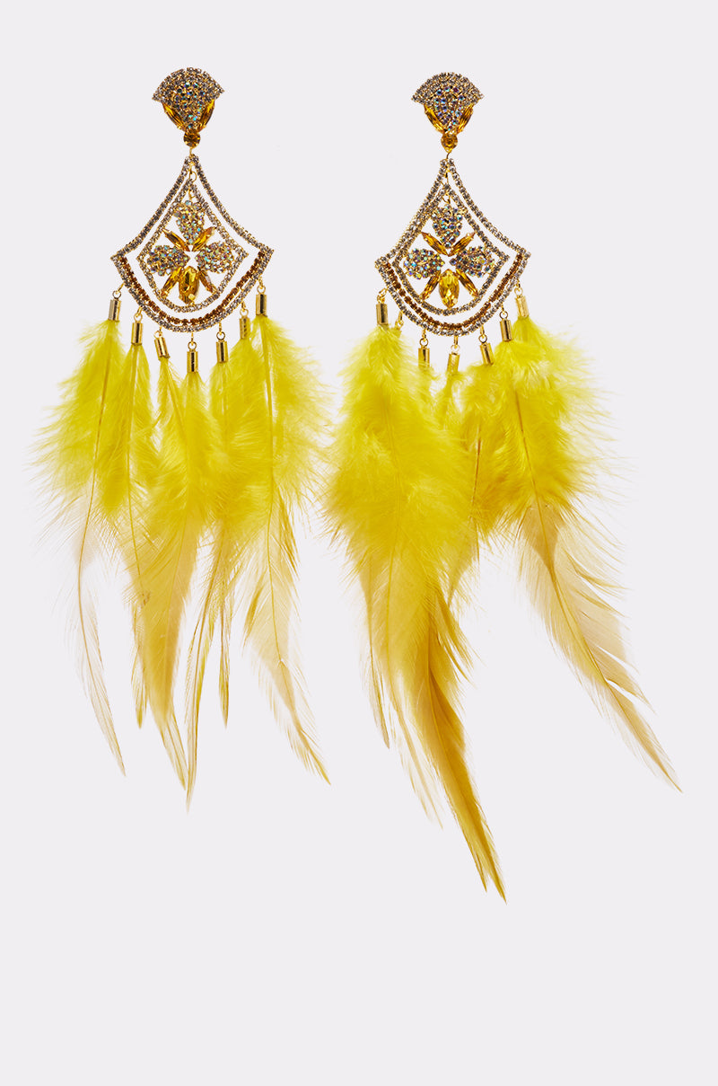 The AT CARNIVALE STATEMENT FEATHER EARRING features gold detailing, sparkling gemstones, and multiple bright yellow feathers, making it perfect festival jewelry. Displayed on a plain white background.