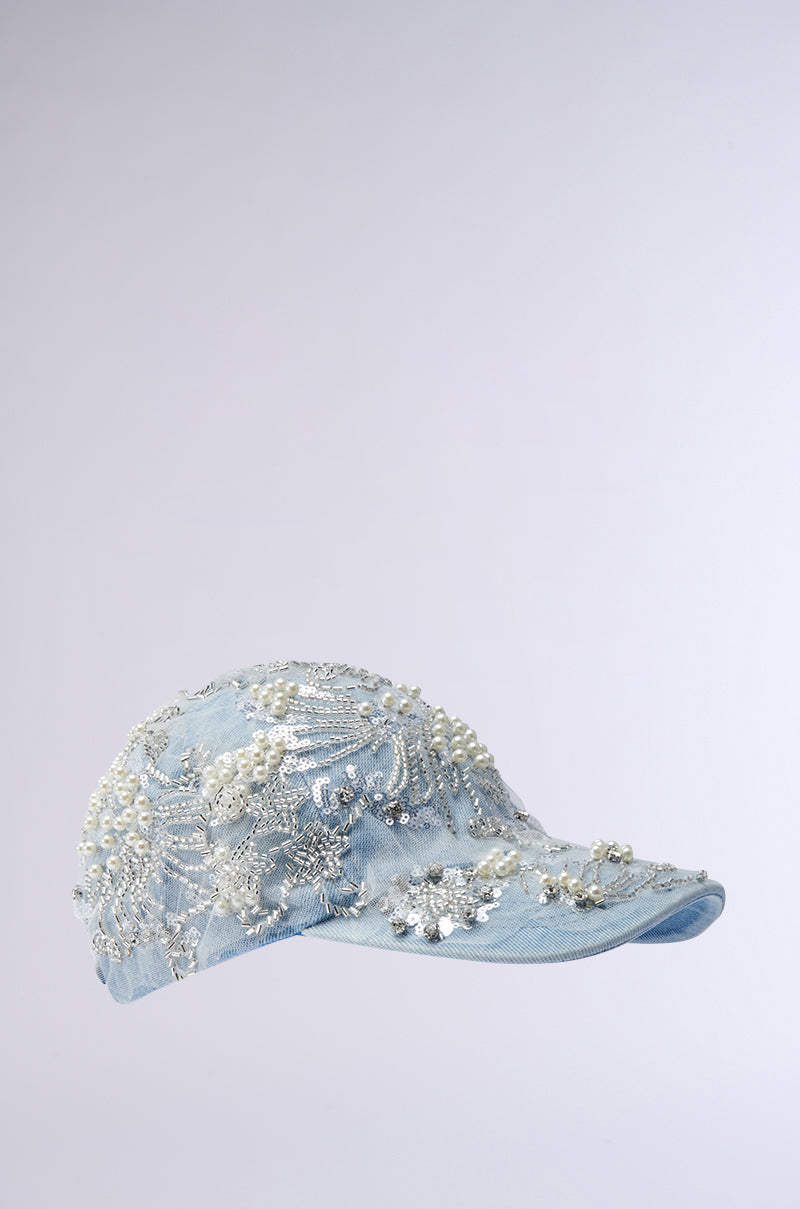 Introducing the BLESSING IN DENIM EMBELLISHED BASEBALL HAT, featuring a light blue denim design beautifully adorned with intricate pearl and bead embroidery in a floral pattern. This chic fashion accessory stands out against a simple gray background. 2