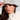 A woman is wearing the BLESSINGS ONLY EMBELLISHED BUCKET HAT in light blue denim, along with hoop earrings. Her long brown hair complements a white textured coat featuring a studded collar. She gazes to the side, gently touching the brim of her stylish hat with one hand.