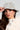 A woman is wearing the BLESSINGS ONLY EMBELLISHED BUCKET HAT in light blue denim, along with hoop earrings. Her long brown hair complements a white textured coat featuring a studded collar. She gazes to the side, gently touching the brim of her stylish hat with one hand.