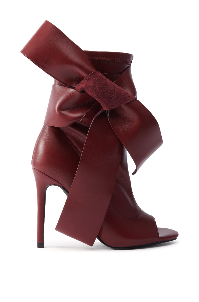 The AZALEA WANG KLARICE BURGUNDY STILETTO BOOTIE is a high-heeled, peep toe bootie in deep burgundy vegan leather with a large decorative bow at the ankle.