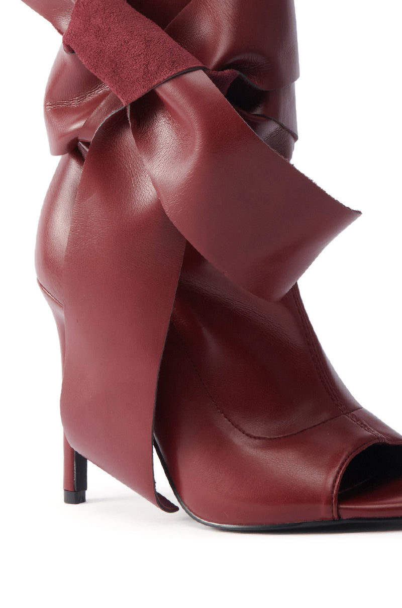 A close-up of the AZALEA WANG KLARICE BURGUNDY STILETTO BOOTIE in vegan leather, showcasing a bold bow at the ankle and a trendy peep-toe design.