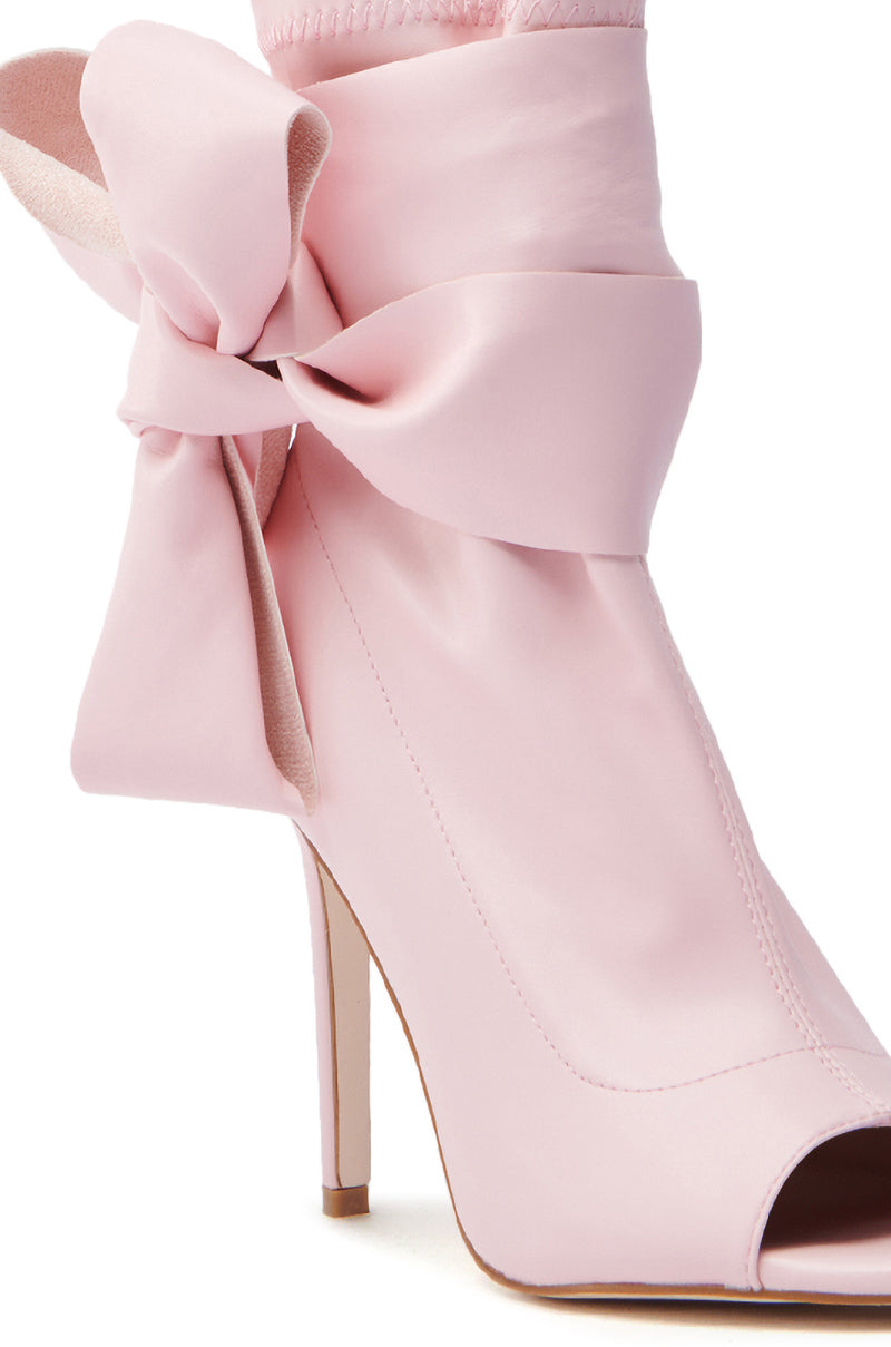 Close-up of the AZALEA WANG KLARICE PINK OPEN TOE BOOTIE: a stylish design featuring a large bow around the ankle, smooth vegan leather texture, and a sleek stiletto heel for a chic look.