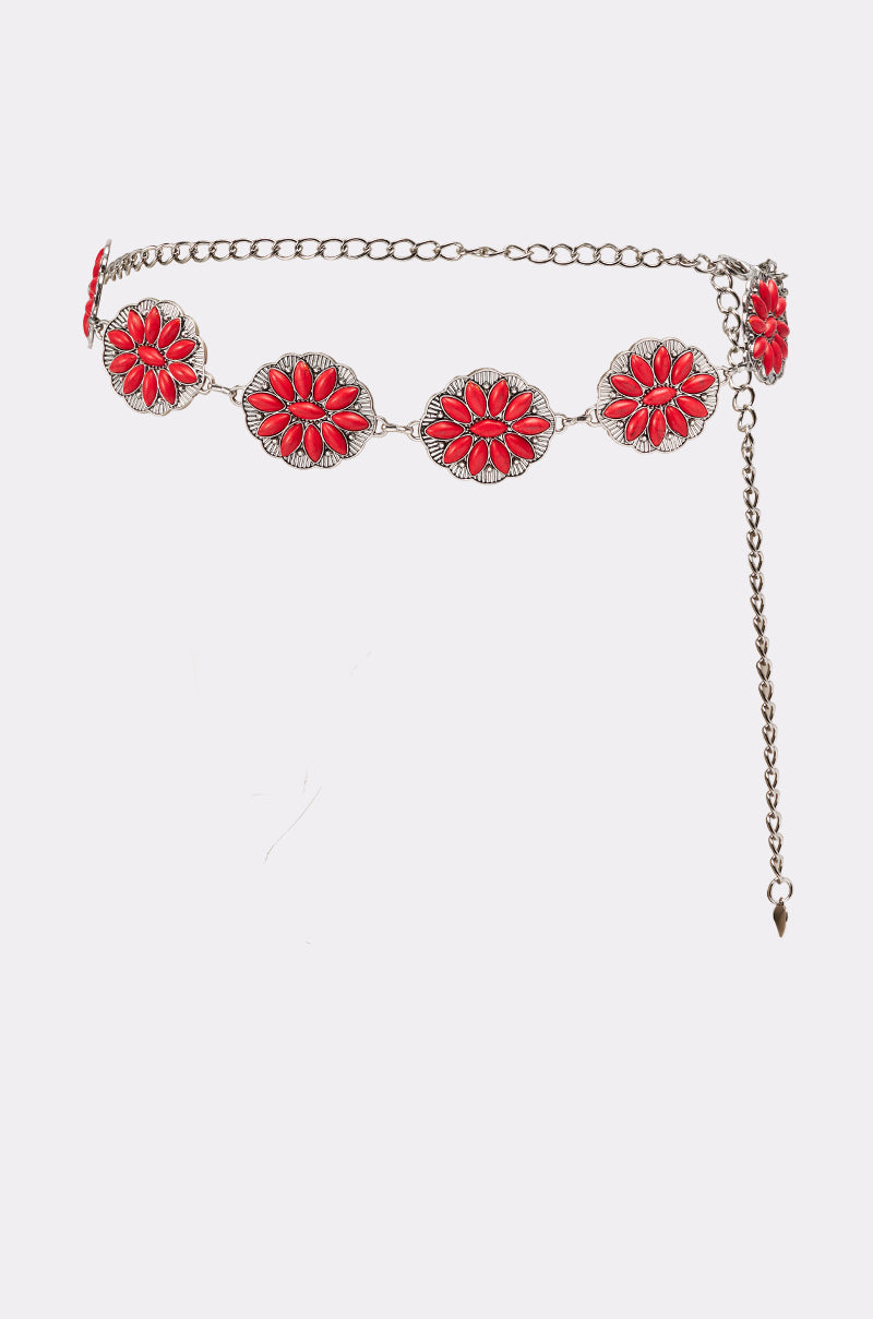 The THRU THE STORM BELT is a silver concho belt with circular red floral medallions, an adjustable dangling chain, and a pointed charm, creating a chic boho statement look. Shown here on a white background. 3