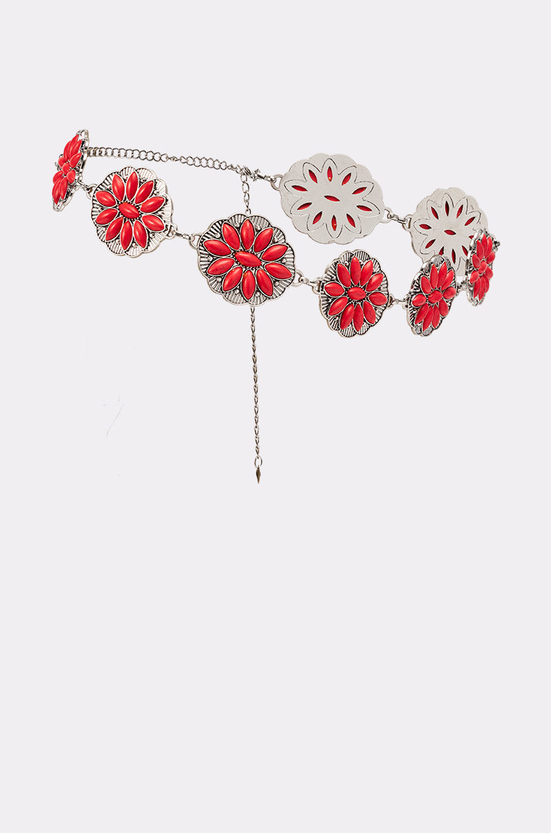 The THRU THE STORM BELT is a decorative silver concho belt with large red and silver flower-shaped ornaments and an adjustable dangling chain, shown against a plain white background. 4