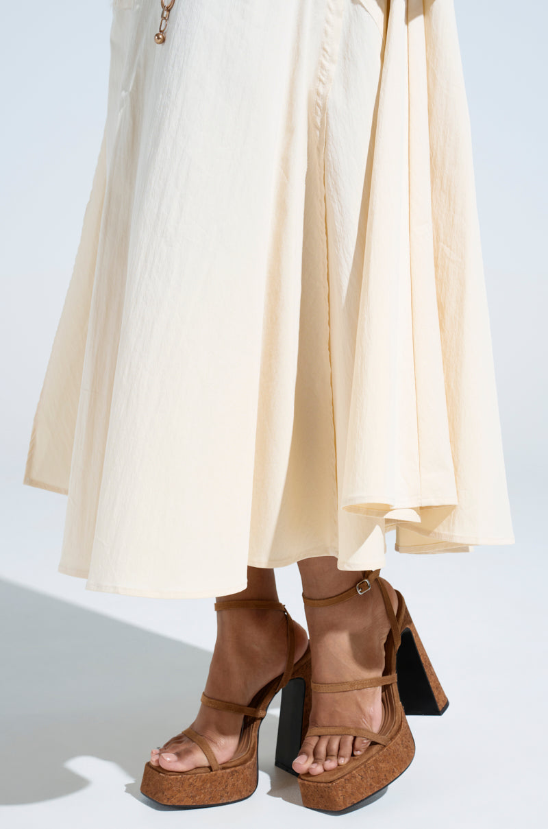 Someone is wearing an off-white, flowing skirt paired with AKIRA Knapp Brown Cork Platform Sandals. The light background adds to the minimalist and elegant vibe.