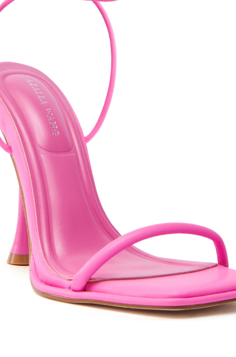 The AZALEA WANG KOHINOOR PINK BOOTIE STILETTO is a vibrant pink, vegan leather sandal featuring a glossy finish. It has a sleek design with a thin toe strap, cushioned footbed, and moderately high, thin heel.