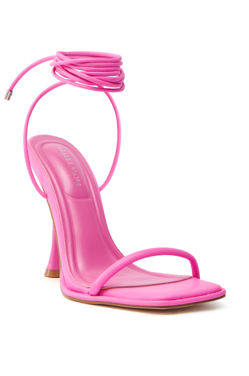 The AZALEA WANG KOHINOOR PINK BOOTIE STILETTO features a vibrant pink vegan leather with a square toe and thin straps. It boasts a rectangular heel, a long coiled ankle strap, and a padded insole for comfort.