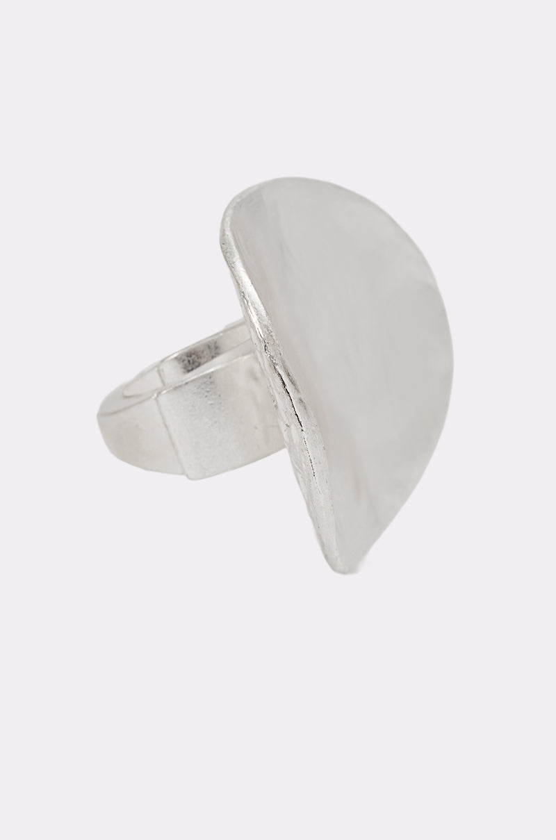 The MOLTEN DREAMS RING is a silver-tone statement piece with a wide, flat, irregularly shaped disc as its centerpiece, set against a plain light background. 1