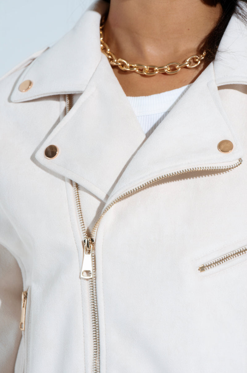 Sporting chic outerwear, they wear the MONTE CARLO FAUX SUEDE MOTO—a white jacket with silver zippers and gold button accents—over a white top. Its boxy cropped silhouette enhances the look, while a gold chain necklace completes their upper-body style.