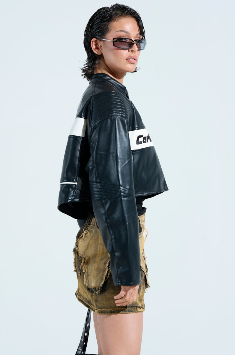 Wearing PRO LEAGUE BOXY MOTO sunglasses and a color block jacket with a white stripe, paired with frayed brown shorts, a person stands in profile against a light blue background. Their short, slicked-back hair complements their assertive pose.