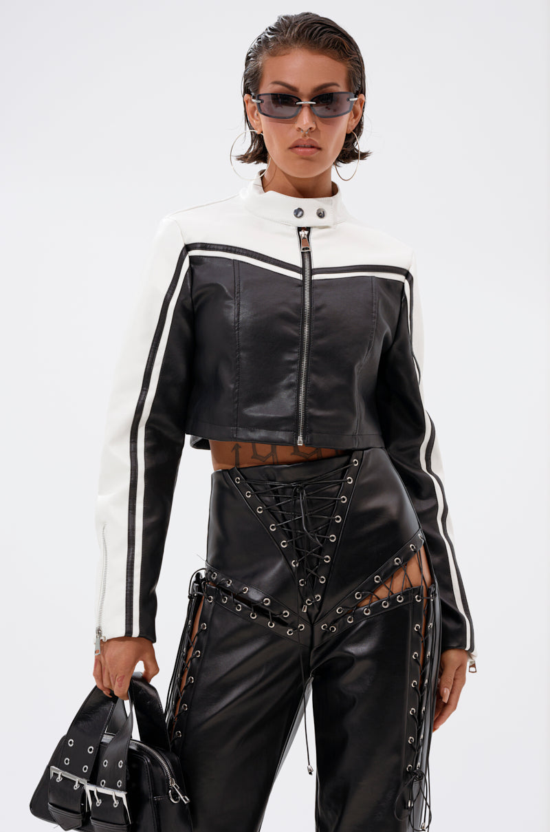Wearing the WEST LOOP RACER MOTO black and white cropped moto jacket, lace-up black leather cutout pants, sunglasses, and holding a small black handbag, this person stands against a plain white background.